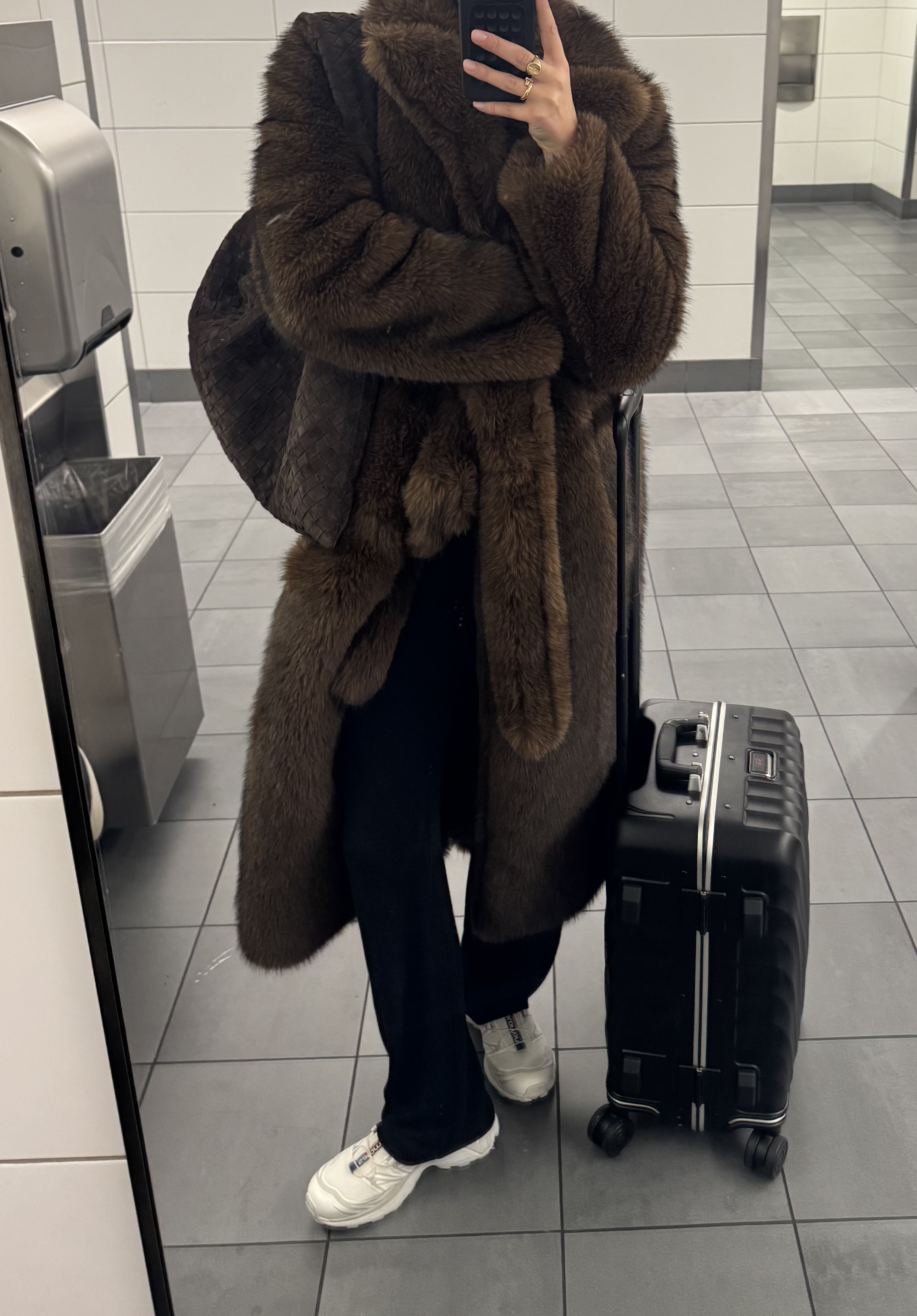 Woman in black sweatpants, fur coat, and Salomon sneakers.