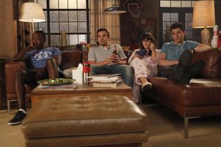 jess and her three male roommates sit on the couch watching tv in their loft on new girl