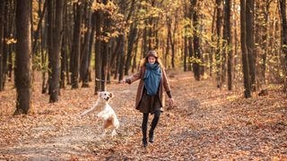 Woman walking through autumn forest with her dog