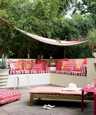 Garden screening ideas illustrated by a fabric canopy hung over built-in seating with red cushions on decking.
