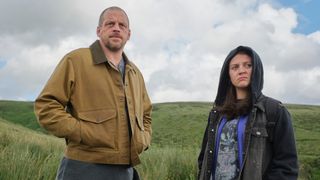 Daniel and Carly in the countryside looking off into the distance with serious looks on their faces