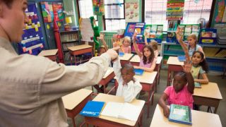 Male teacher points to child raising hand in classroom