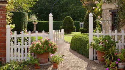 white picket fence and decorative gate leading to a cottage garden