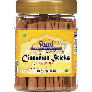 A clear plastic jar of cinnamon sticks stacked vertically with a gold screw top lid