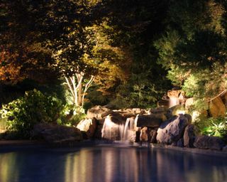 pool lighting illuminating rock boulders and mini waterfalls around a pool