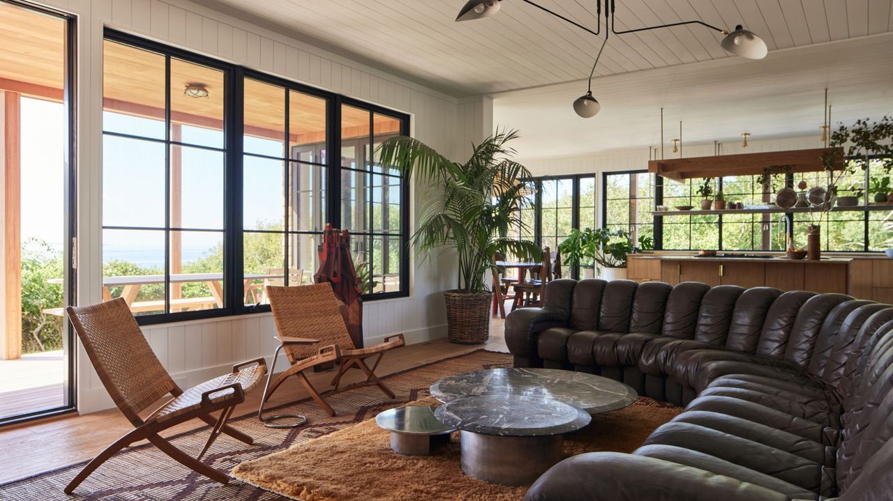 living room with large black leather sofa, white walls, and earthy color palette furniture