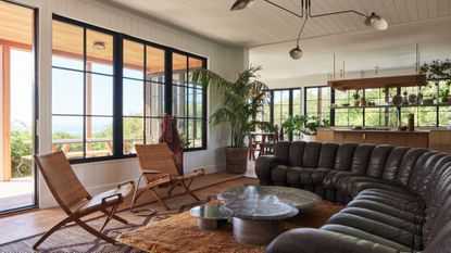 living room with large black leather sofa, white walls, and earthy color palette furniture