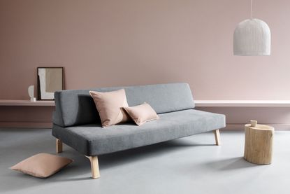 Minimalist design with chalky pink wall with floating bench attached, pink chushions and a grey sofa, tree stump coffee table