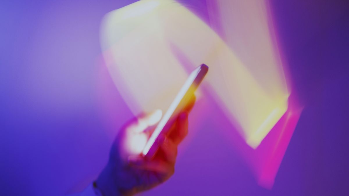 Closeup of a hand using a smartphone on a holographic purple background