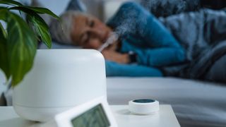Woman sleeping late at night with alarm clock and air humidifier on bedside table