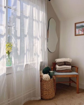 Corner of a cozy bedroom with sheer drapes, casually styled chair and wool yarn