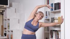Woman in sports bra and leggings performs a side stretch in front of a bookcase