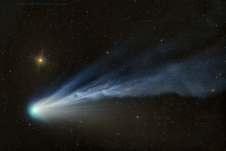 a vibrant blue comet and dusty tail streak across the whole image before a dark, starry space and a shining distant star.