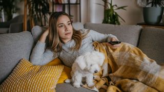 woman and dog on sofa with blanket watching tv