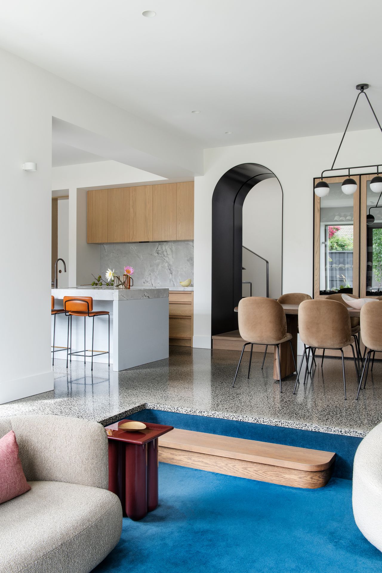 open plan room with kitchen, dining room, terrazzo floors, and sunken living room with bright blue carpets