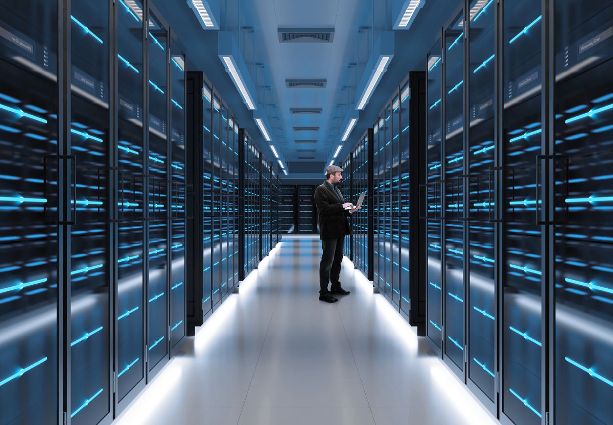 Data centers stock image showing a worker on laptop in a server room 