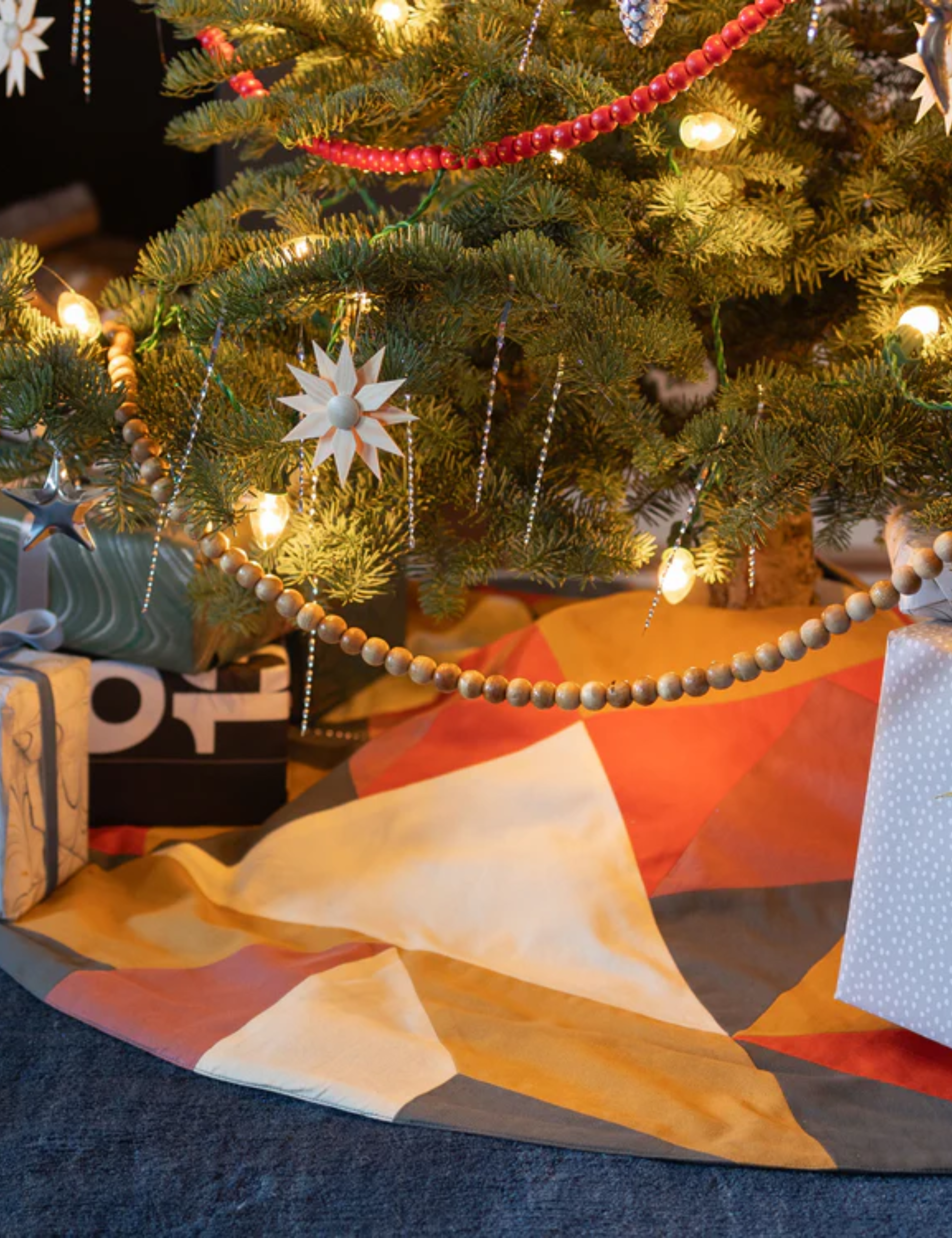 Wooden beaded garland draped at the base of a Christmas tree, which is styled with a colorful geometric tree skirt