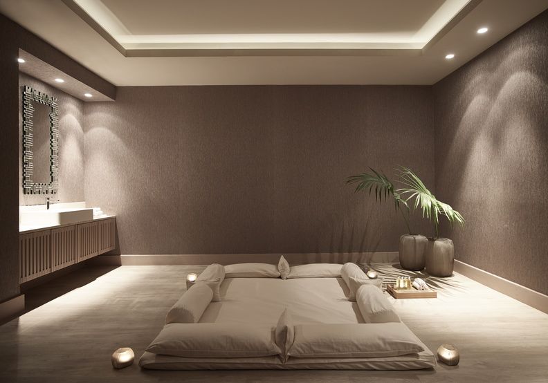 A picture of a treatment room in Sani Resort, it's decorated with muted stone colours and is lit by candles. The treatment bed is in the middle of the room