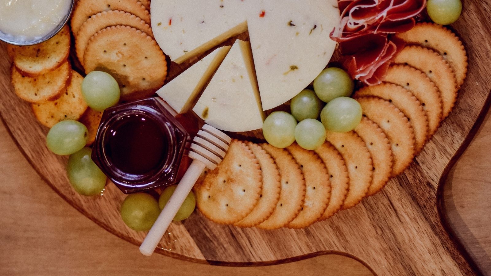 Charcuterie board with meat, cheese. crackers, grapes and honey