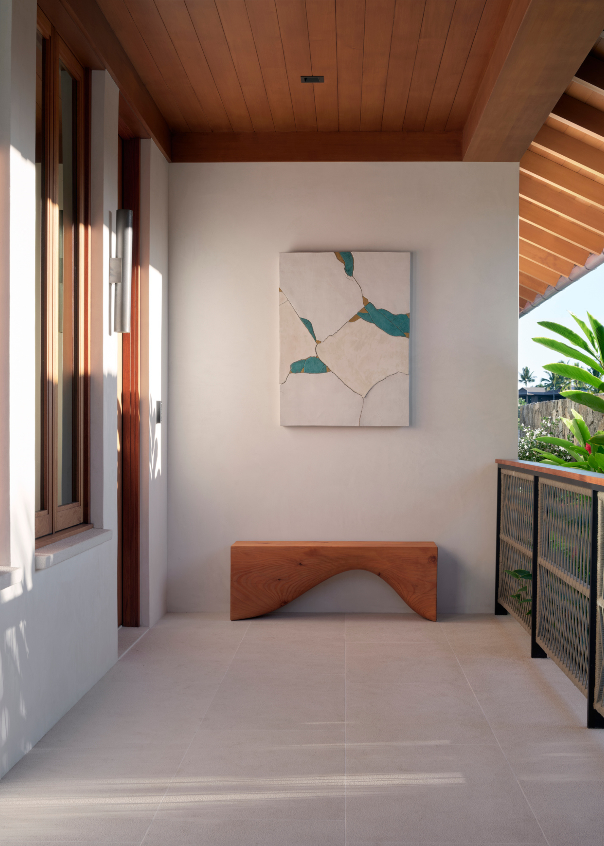 A balcony with a sculptural wood bench and hanging art
