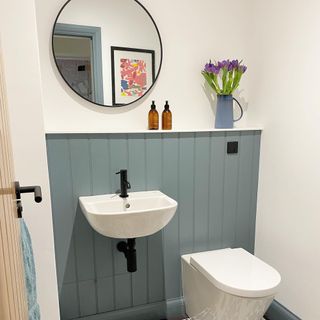 White painted bathroom with hanging circle mirror and teal accents