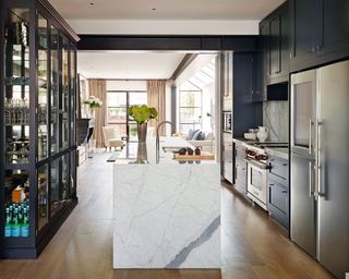 Kitchen storage ideas showing an open plan kitchen with a marble effect island and glass front cabinets on one side