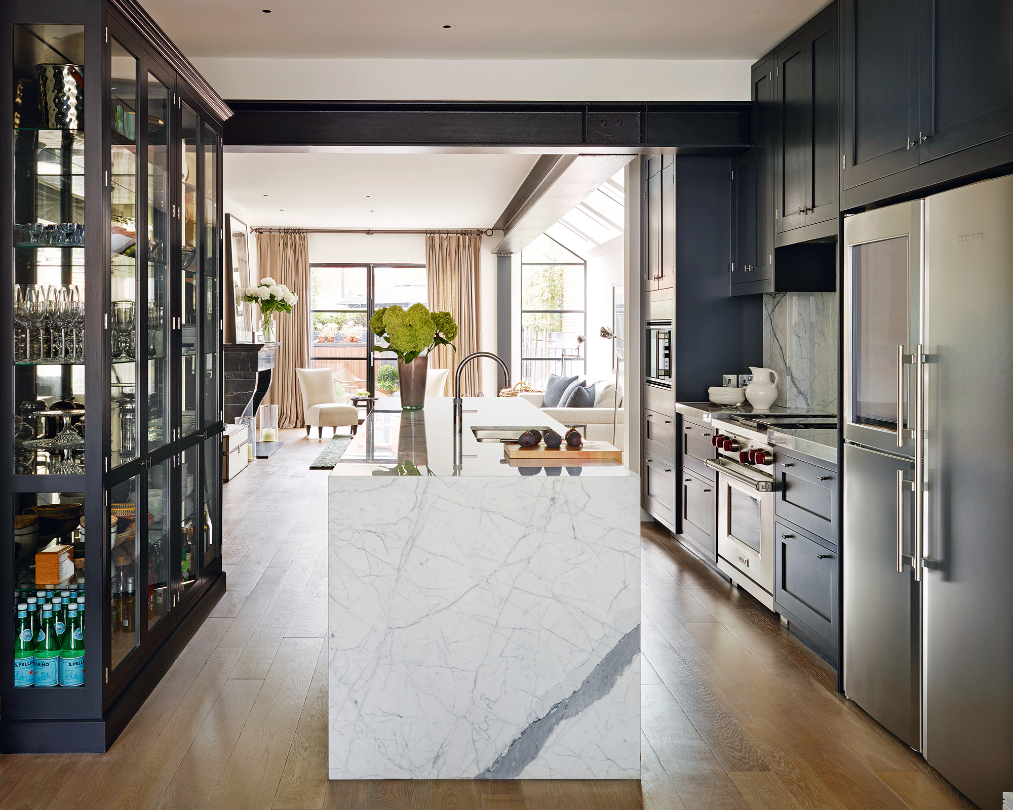 An example of galley kitchens in an open plan layout, with dark blue cabinetry and white marble island.