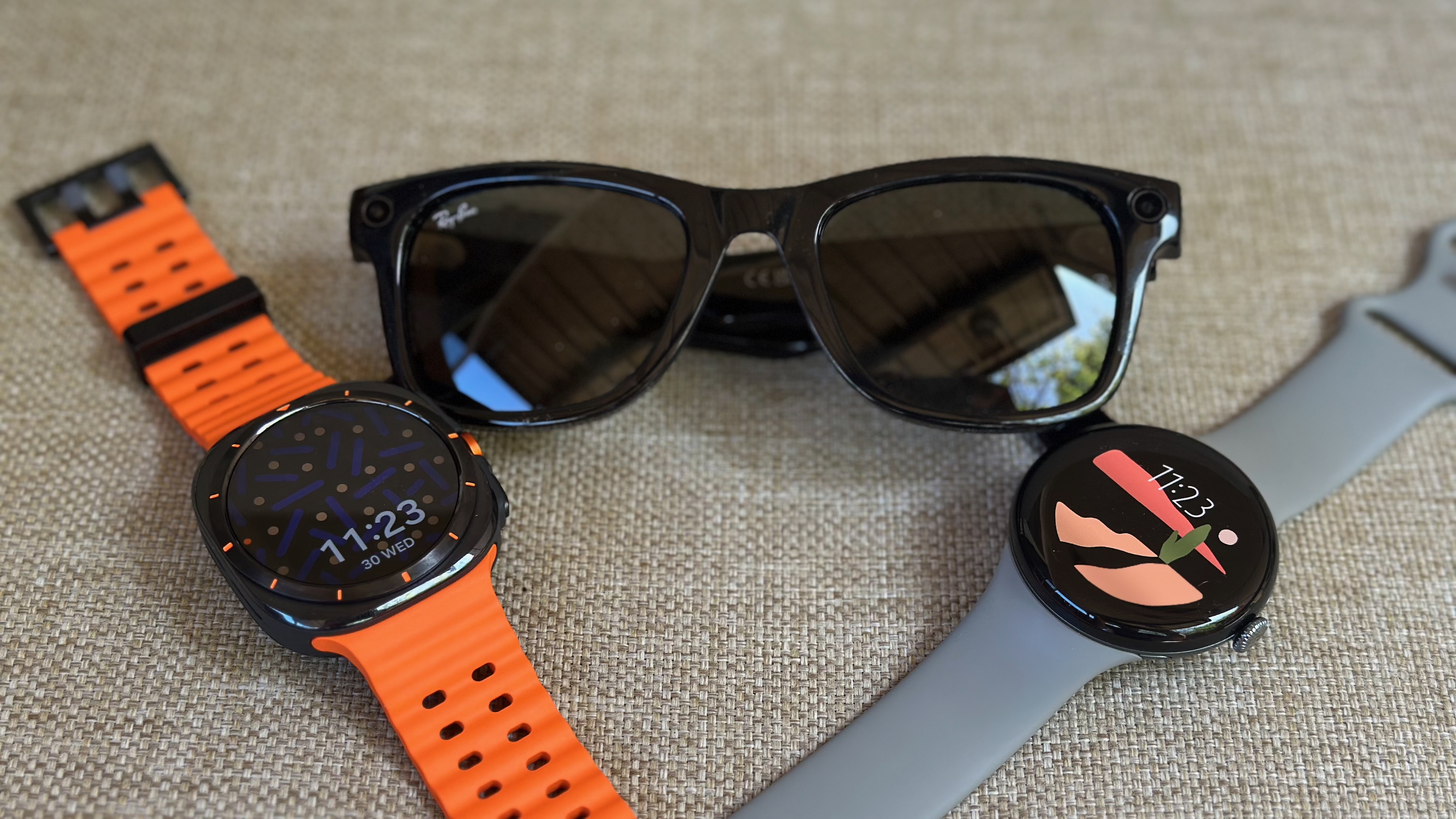 The Samsung Galaxy Watch Ultra (left) and Google Pixel Watch 3 (right) sitting at diagonal angles next to Ray-Ban Meta smart glasses (center).