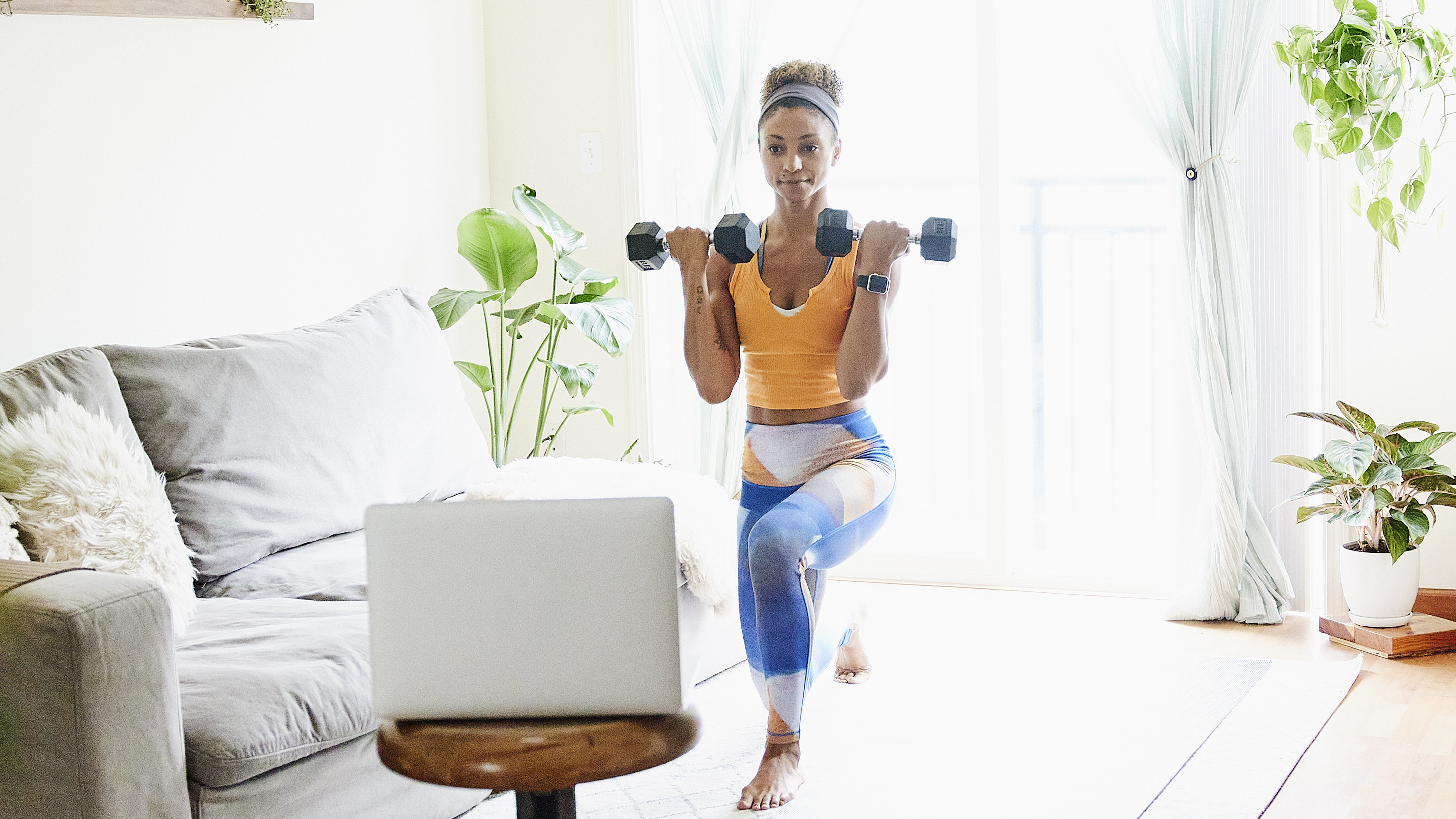 Woman exercises with dumbbells in front of a laptop in a living room