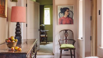Pale pink entryway with dark wooden sideboard, dark wooden chair and painting of a woman above.