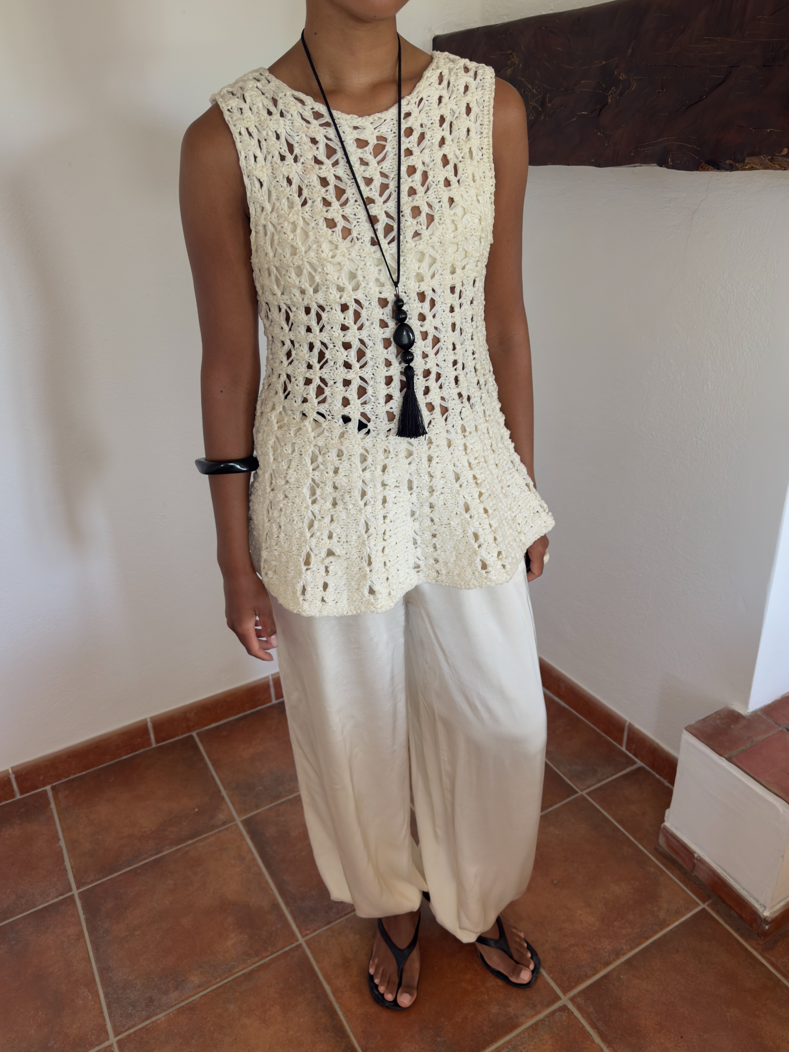 An image of an influencer wearing a sleeveless crochet top, white balloon trousers and black heeled flip-flops
