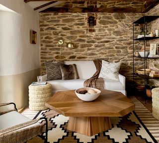 A modern rustic living room with octagonal wooden table, geometric rug and stone feature wall