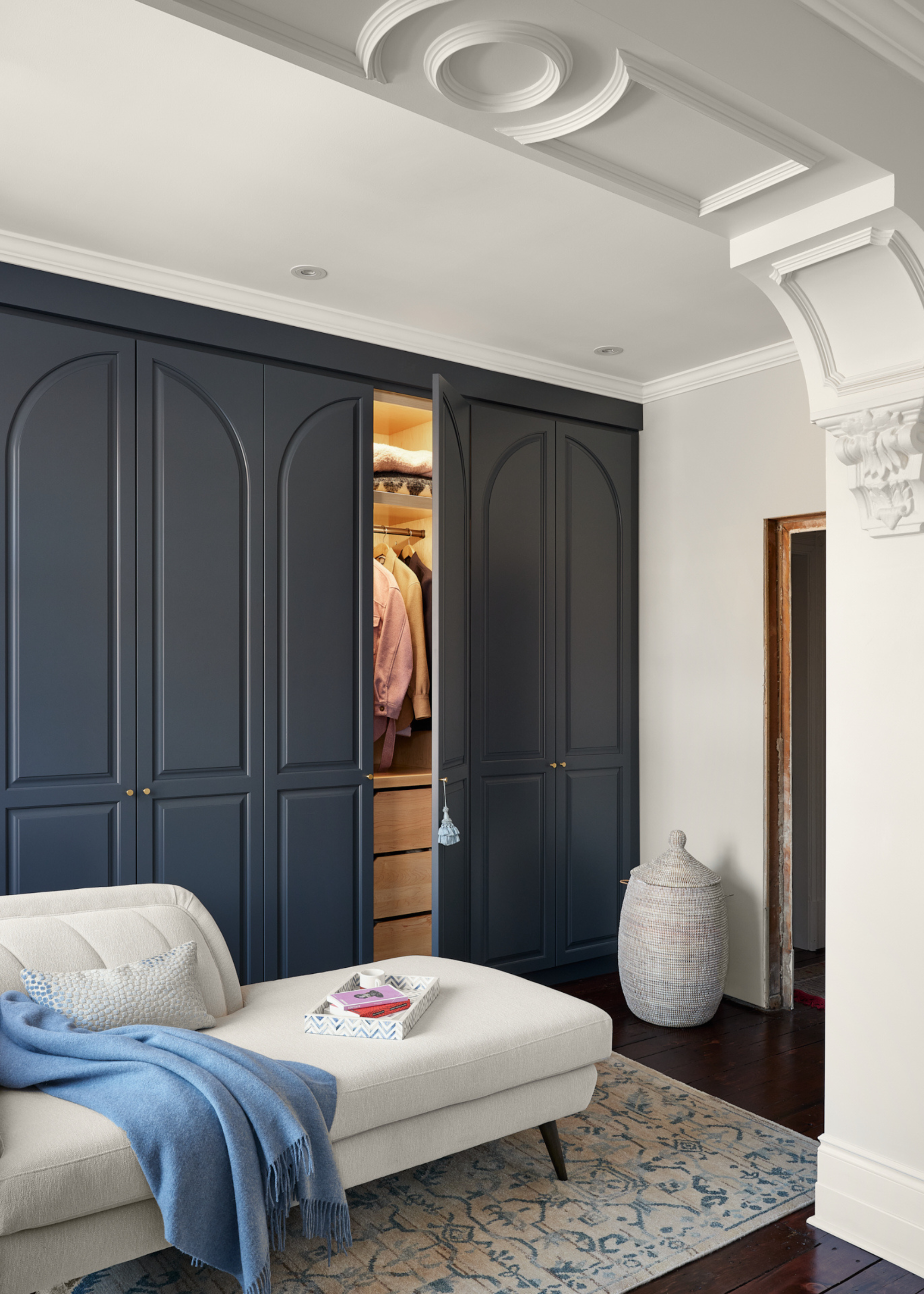 A bedroom with a fainting couch and an open wardrobe door showing the inside of a lit closet