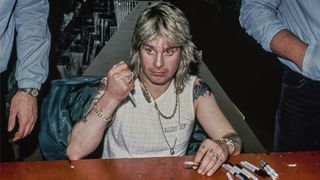 Heavy metal singer Ozzy Osbourne seated at a table during an autograph session, 1st March 1984, during the Ozzy/Motley Crue tour