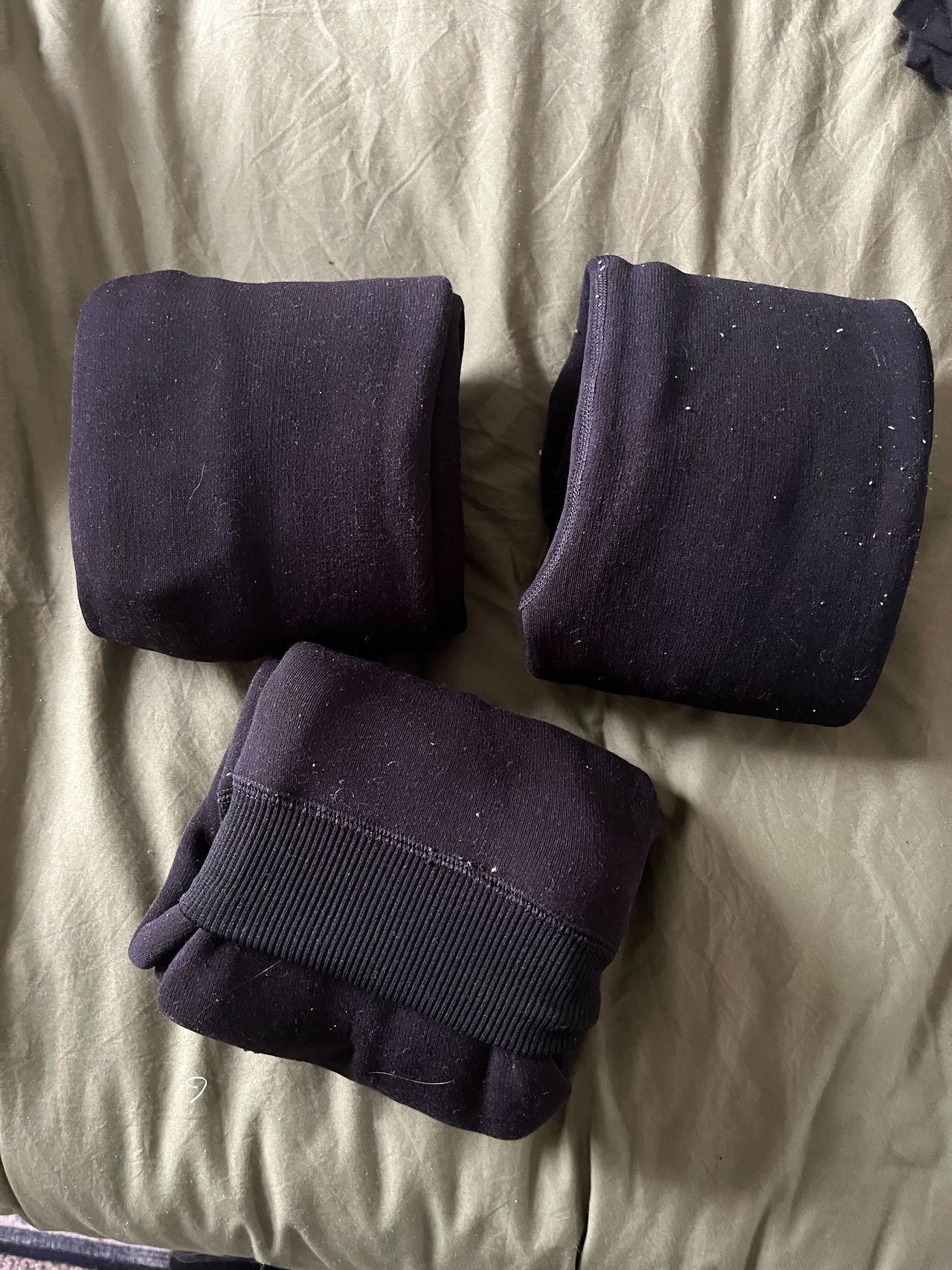 Three pairs of black leggings folded in thirds on a green bed