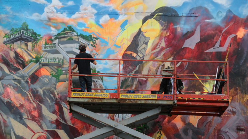 Man on a cherry picker painting a mural
