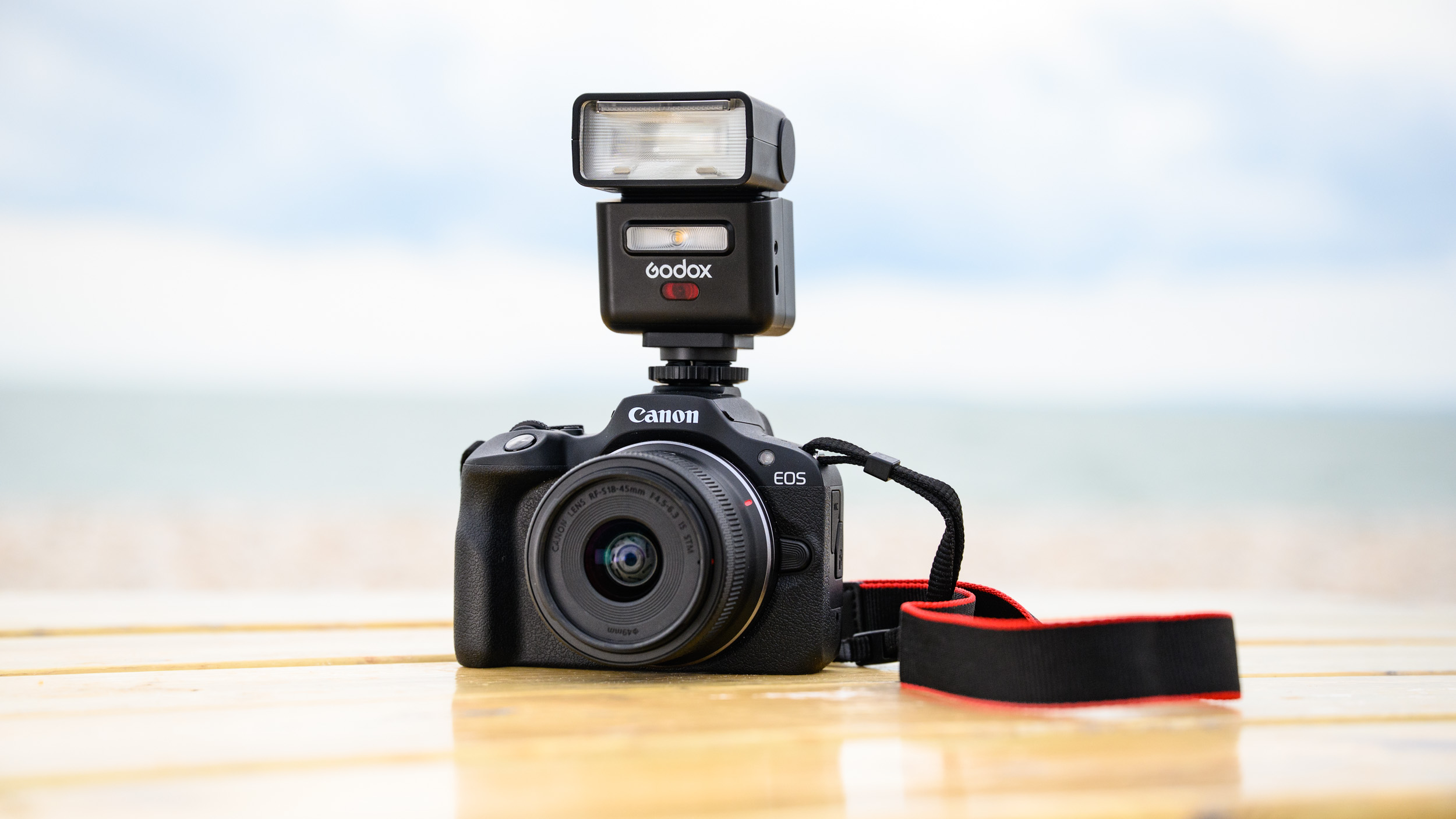 Godox iT32 camera flash attached to a Canon camera and placed on a wooden seaside bench, the ocean is behind it