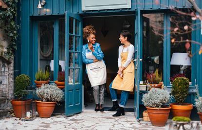 Happy African-American woman and her employee talking and laughing while standing at door of the store.