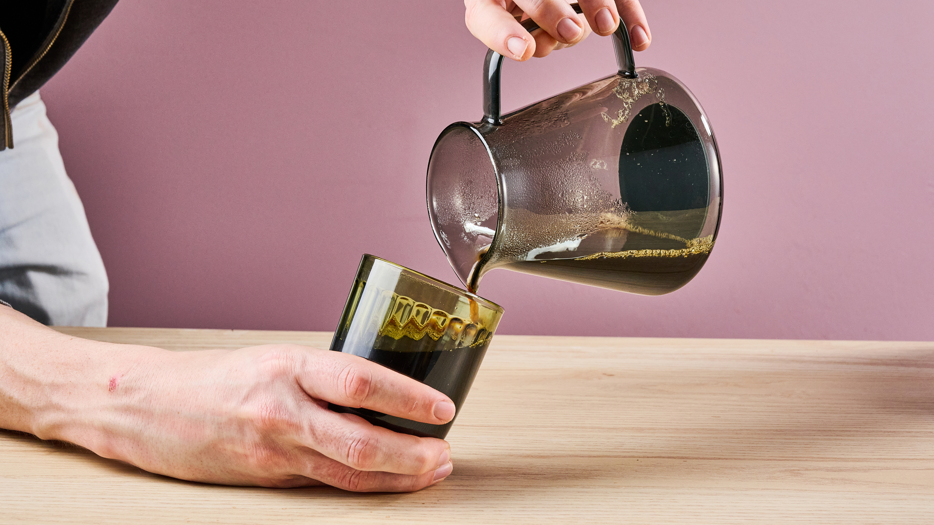 A man pours rich black coffee out of the Ratio Four's carafe into a glass.