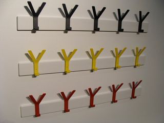 3 rows of 5 Y shaped wall hook on a white wall. The hooks on the top row are black, middle row is yellow and bottom row is red.