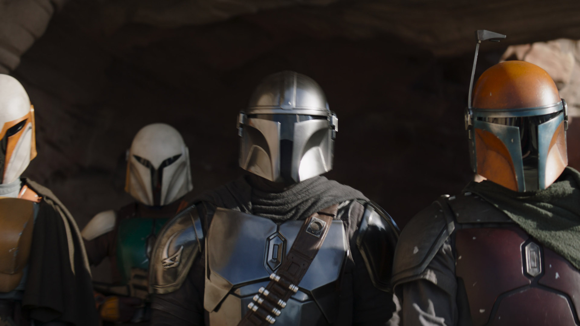 Din Djarin stands in a desert location looking at something off screen alongside his fellow Mandalorians in season 3