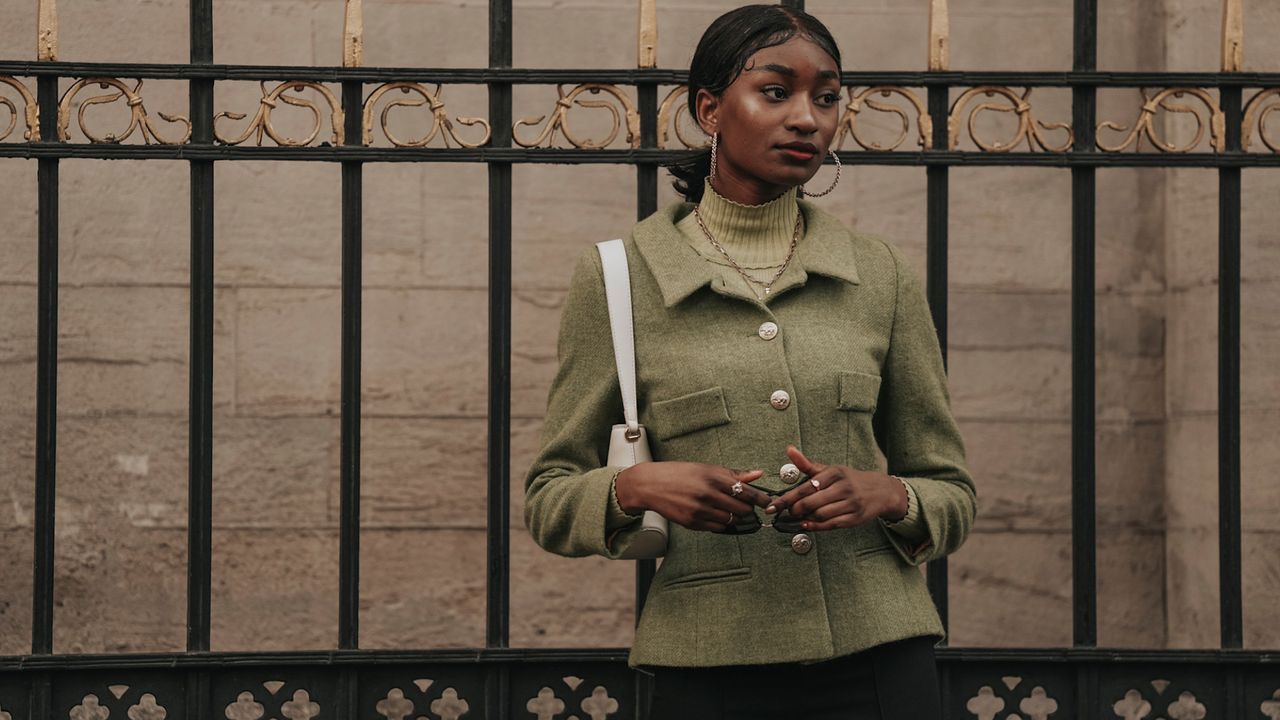 a paris fashion week attendee wearing a green fitted blazer gold hoop earrings turtleneck sweater and white shoulder bag 