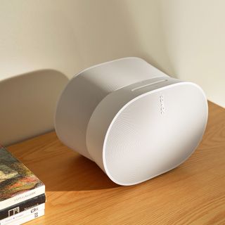 White Sonos speaker on a wooden table with cream wall behind