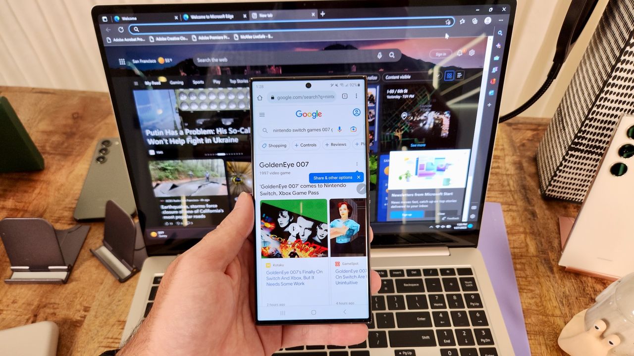 The Samsung Galaxy S23 Ultra, showing the Chrome web browser, held in front of the Samsung Galaxy Book 3