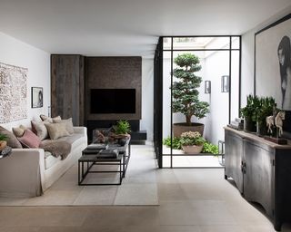 A large Japandi style basement living room, with a large floor to ceiling window into a small sunken courtyard with Japanese plants inside.