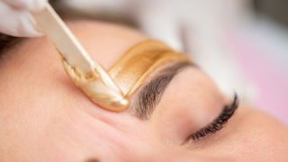 Gold wax being applied above eyebrow with beauty spatula