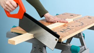 Person sawing wood secured on workmate with a tenon saw 