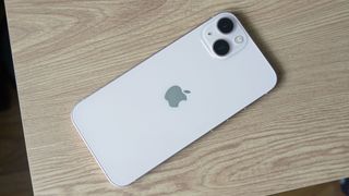 Un iPhone 13 en blanco sobre una mesa de madera