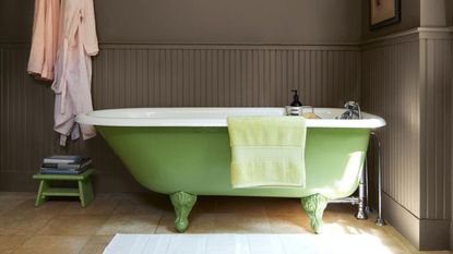 A bathroom with brown walls, paneling, and a lime green freestanding bath tub