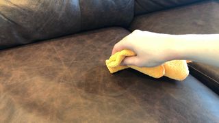 A leather couch being cleaned with a damp microfiber cloth